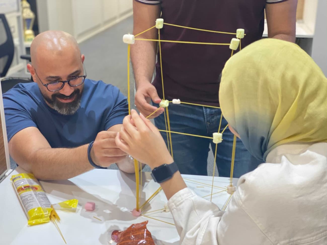 Colleagues building the spaghetti and marshmallow tower.